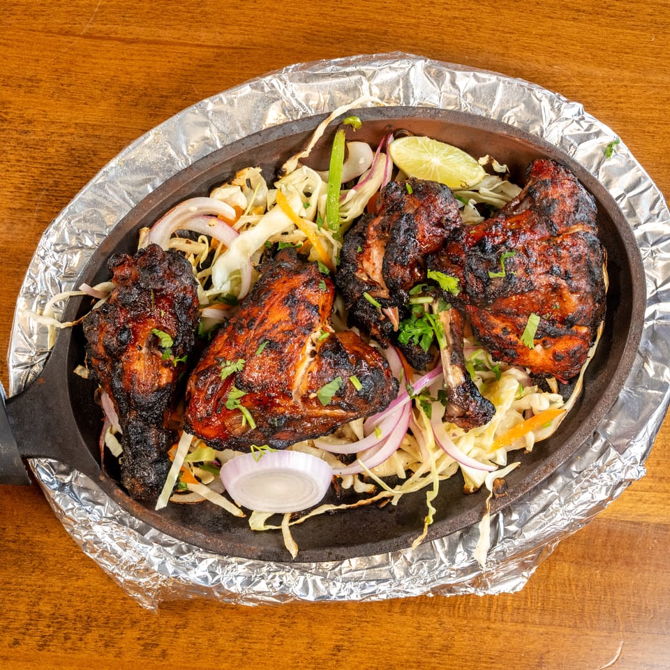 Tandoori chicken drumsticks and thighs with sliced onions, cabbage, and lime in a sizzling skillet.