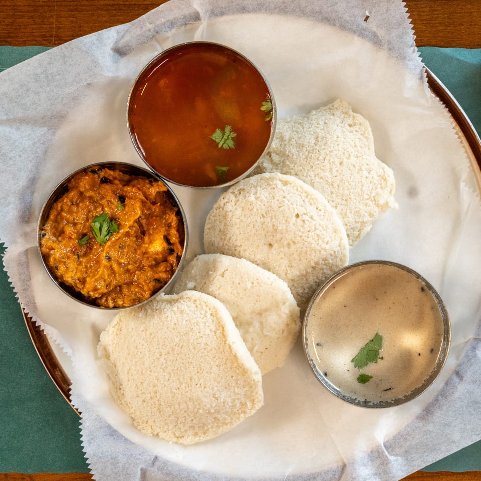 Overhead view of a South Indian thali with idli, sambar, chutney, and a spicy side dish.