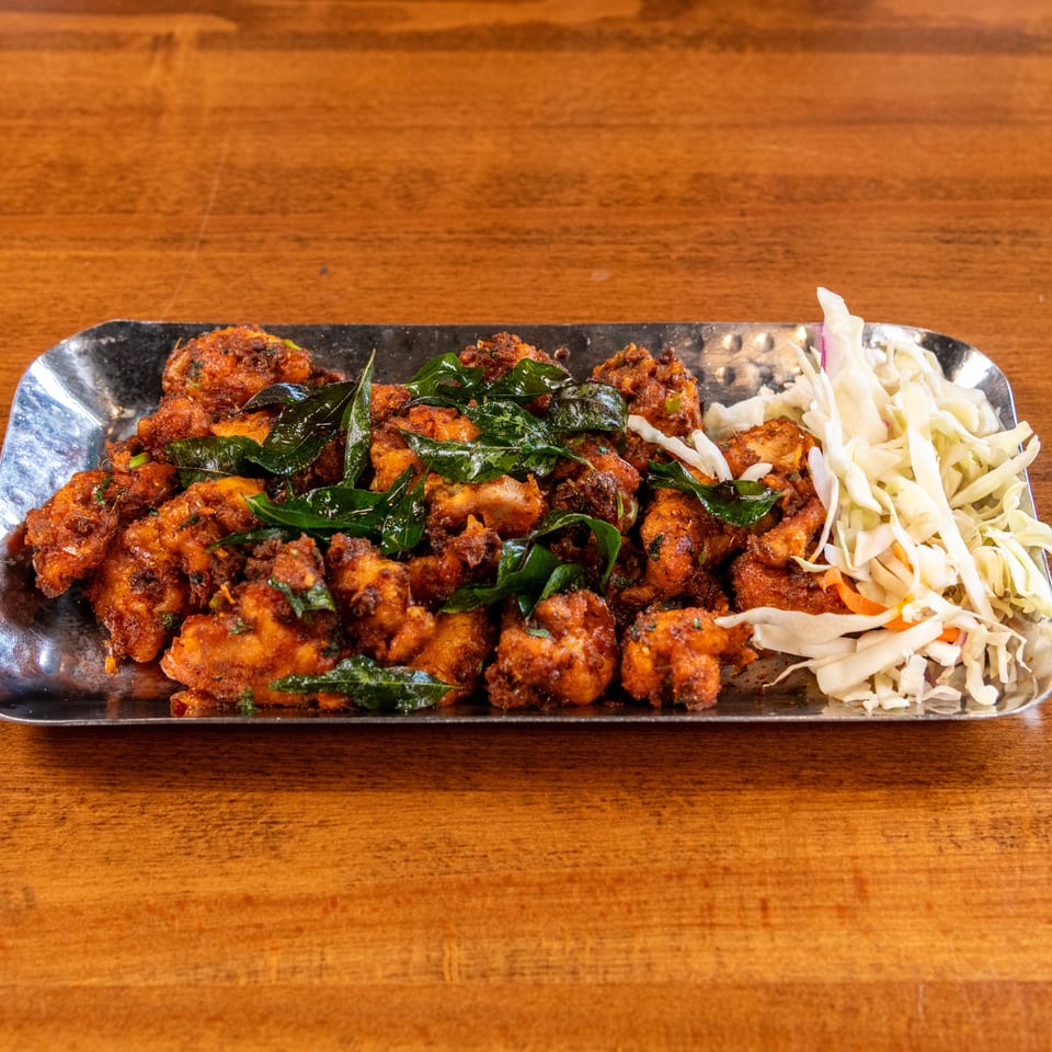 Crispy fried chicken pieces with green herbs and shredded cabbage on a silver platter.