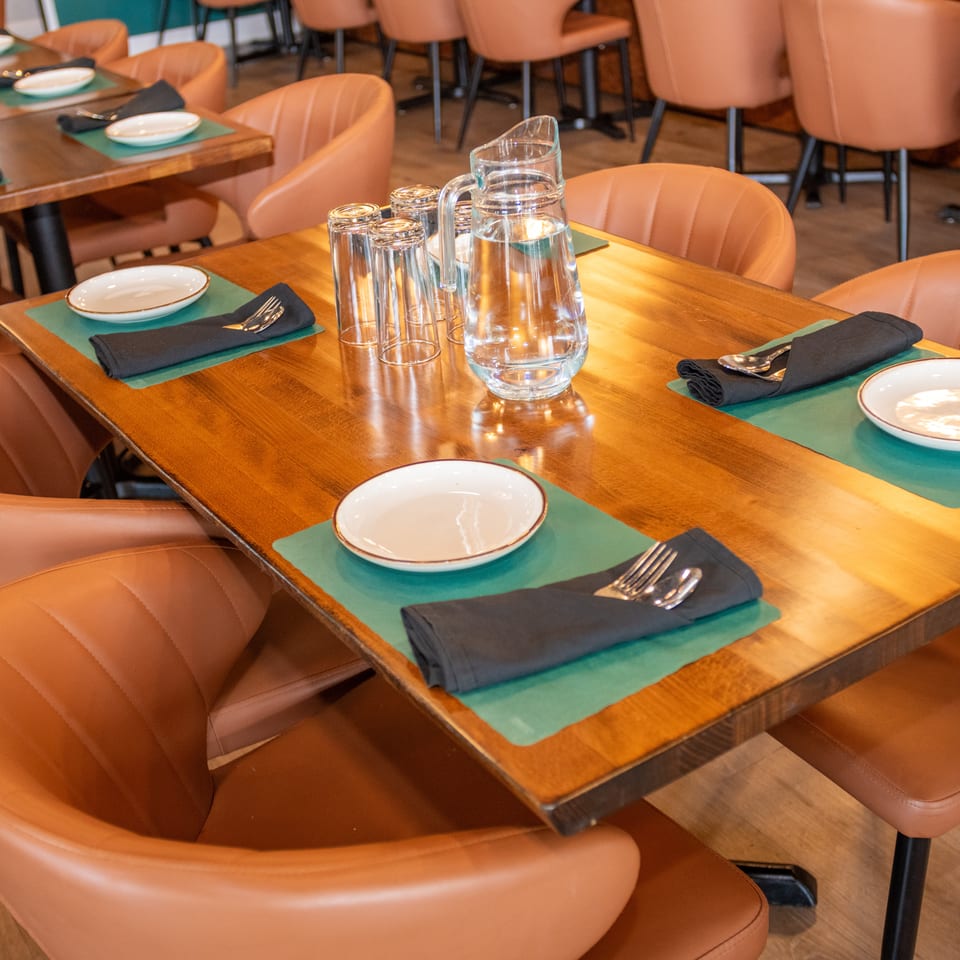 A restaurant dining room with wooden tables, brown leather chairs, and place settings with water pitchers.