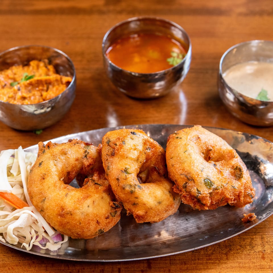 Three golden-fried vada donuts with shredded cabbage salad and three small bowls of dipping sauces.