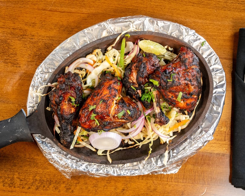 Tandoori chicken legs with onions, cabbage, and lime in a sizzling cast iron pan.