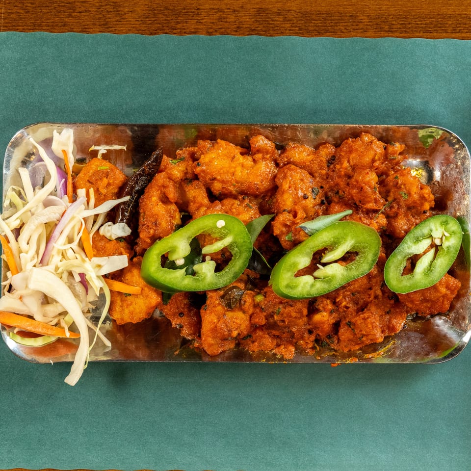 Overhead view of a metal tray filled with orange chicken, sliced green peppers, and a side salad.