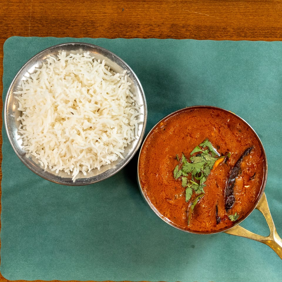 Overhead view of a bowl of white rice and a pot of red curry with cilantro.