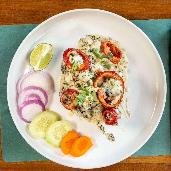 Creamy chicken dish with red onion rings, cilantro, and a side of sliced vegetables.