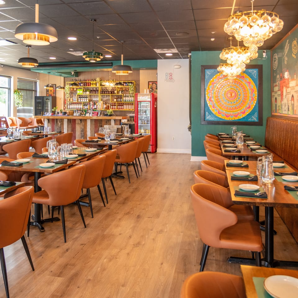 An empty restaurant dining room with brown chairs, wooden tables, a bar, and colorful wall art.