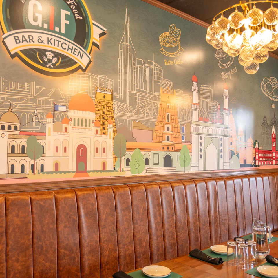 Restaurant interior with brown leather booth seating, set tables, and a colorful mural of cityscapes and food.