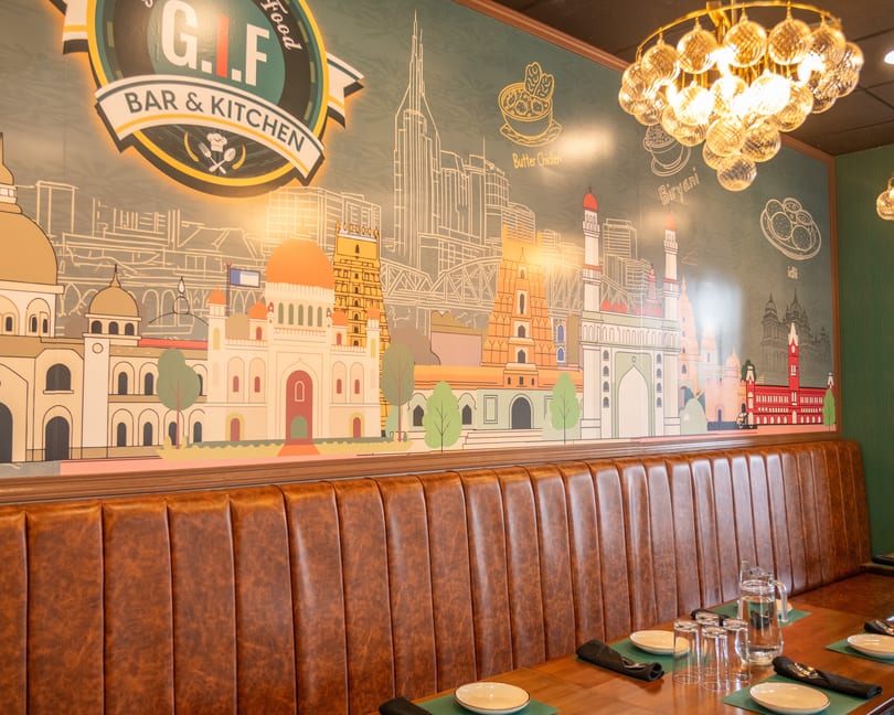 Restaurant interior with brown leather booth seating, set tables, and a colorful mural of cityscapes and food.