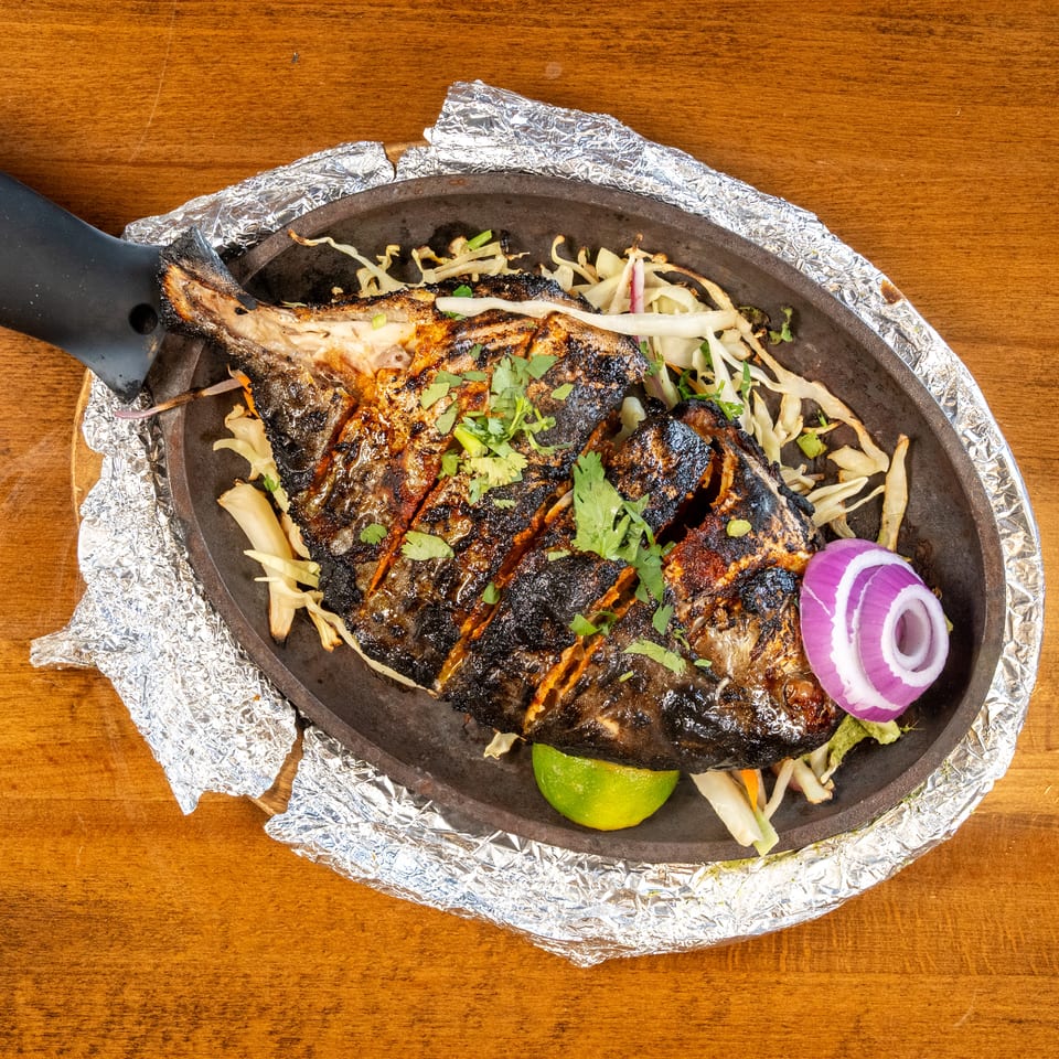 Grilled whole fish with herbs, lime, and red onion on a sizzling platter with foil.