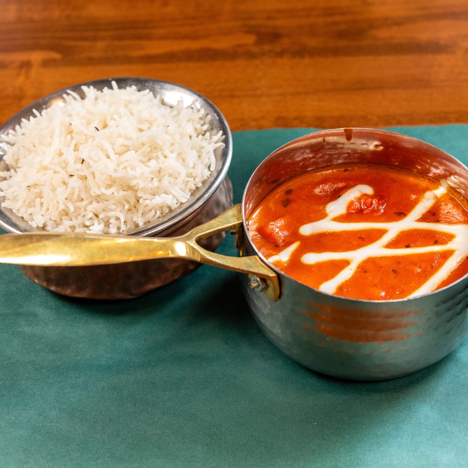 A metal bowl of white rice and a small metal pot of orange curry with white cream swirls.