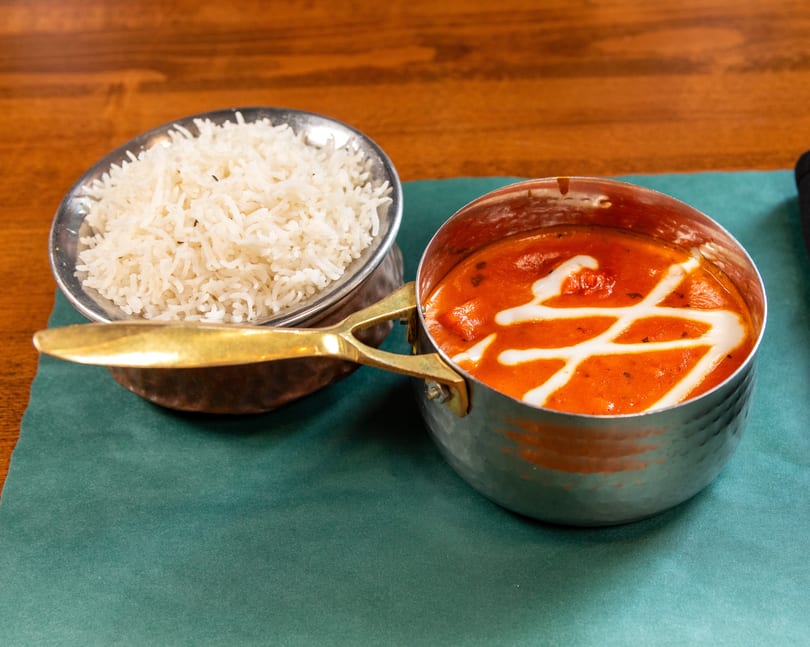A metal bowl of white rice and a small metal pot of orange curry with white cream swirls.