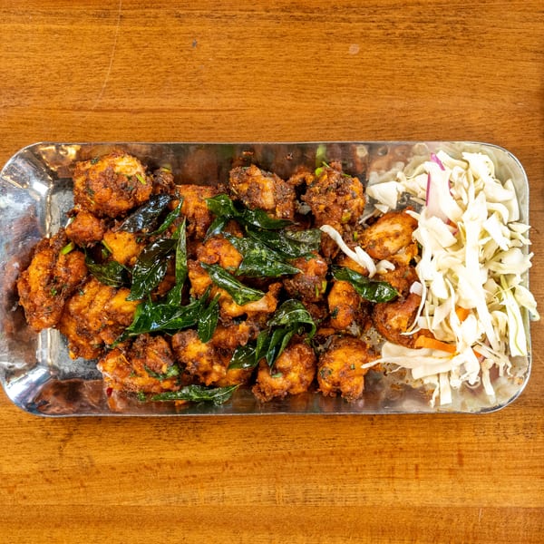 A metal platter of fried chicken pieces with curry leaves and a side of shredded cabbage.