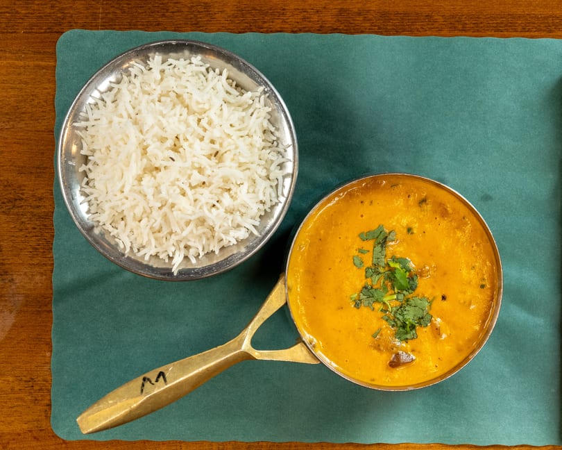 Overhead view of a golden curry with cilantro and white rice in metal bowls on a green placemat.