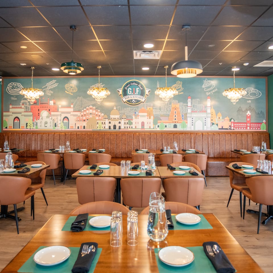 The Great Indian Food Bar & Kitchen dining room features a mural, brown booths, and set tables.