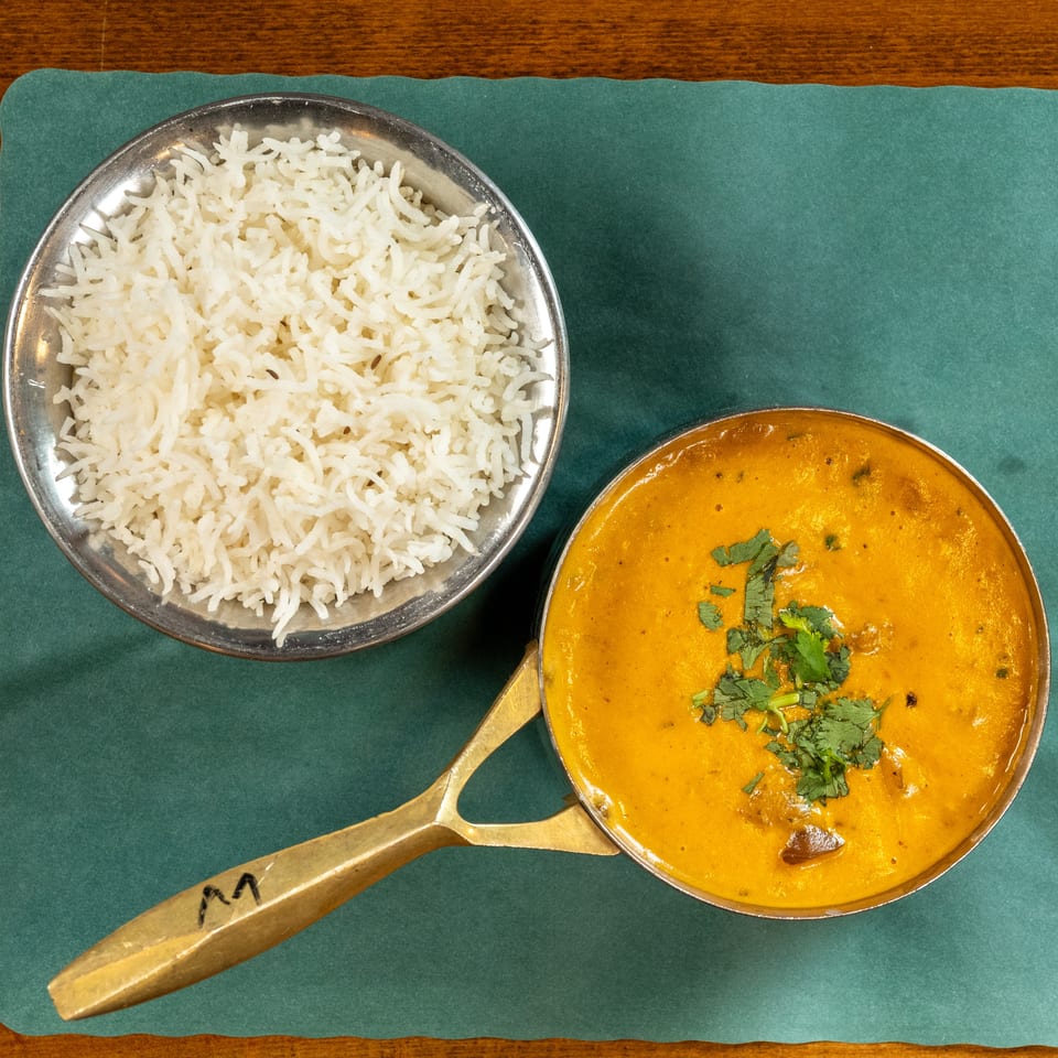 Overhead view of a bowl of white rice and a pot of yellow curry with cilantro on a green placemat.