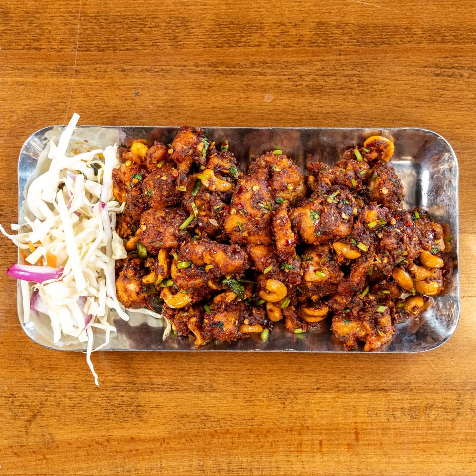 Spicy fried chicken with cashews and fresh cabbage salad on a metal tray.