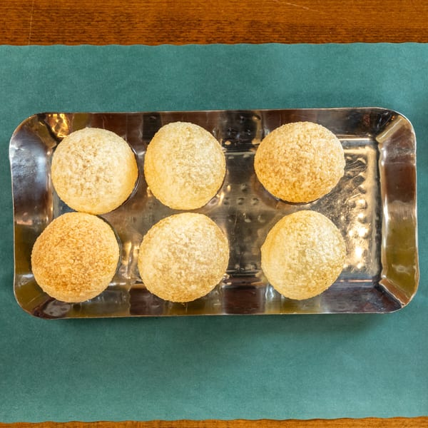 Six golden-brown pani puri shells arranged on a rectangular silver tray, on a green placemat.