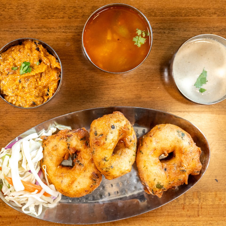 Three golden-brown medu vada, shredded cabbage salad, and two bowls of chutney on a wooden table.