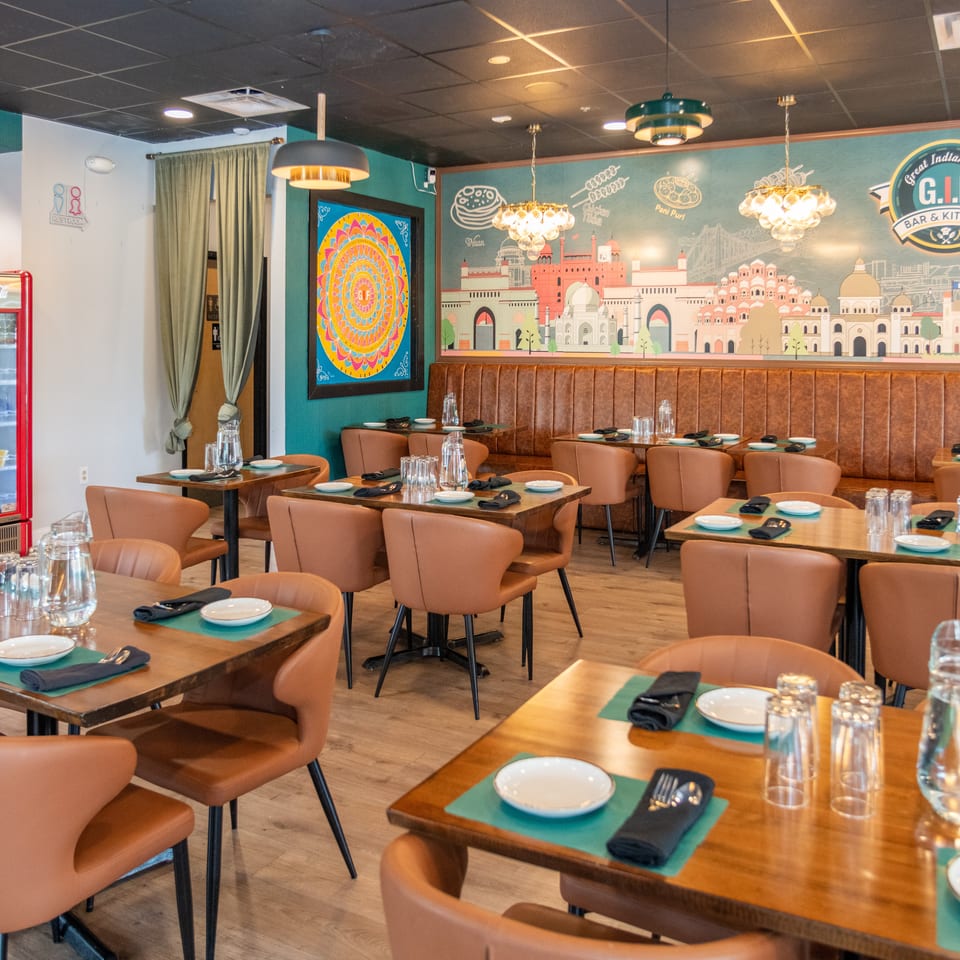 Interior of GIF Bar & Kitchen, an Indian restaurant, with empty tables, brown chairs, and a colorful mural.