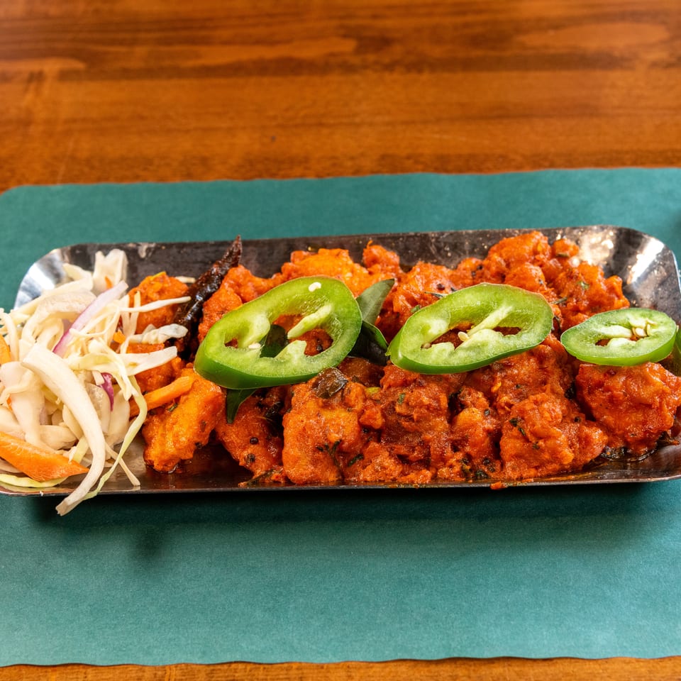 Spicy orange chicken dish with green peppers and a side of pickled vegetables on a metal tray.