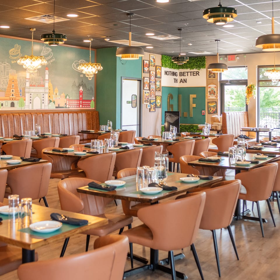 Modern Indian restaurant interior with brown leather seating, set tables, and a cityscape mural.