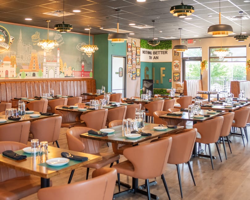 Modern Indian restaurant interior with brown leather seating, set tables, and a cityscape mural.